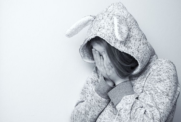 Photo of child in a hood with ears, holding their head in their hands