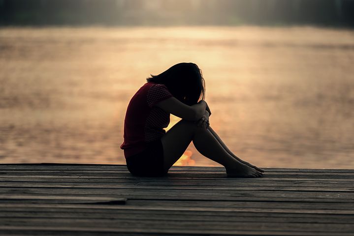 Photo of a child sitting on the edge of a pier with their knees up, and their arms and head resting on their knees