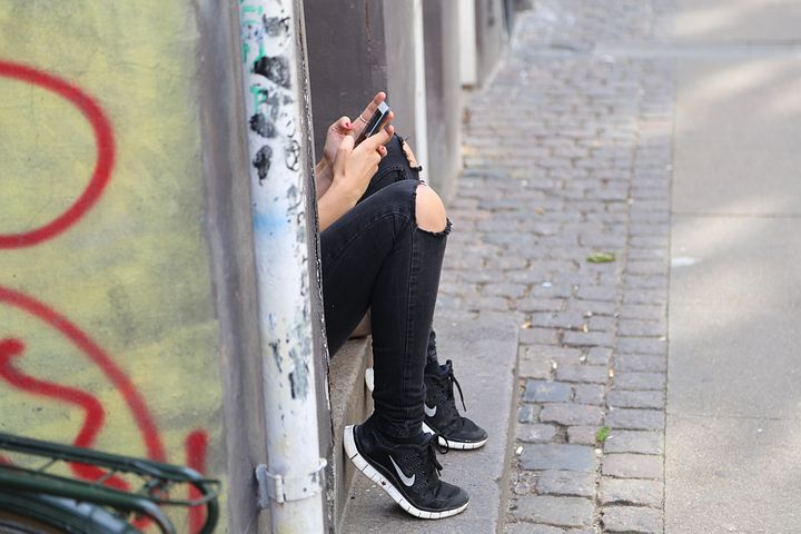 Photo of a street with a teen sitting on a stoop on their phone